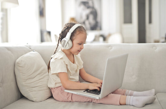 little girl works with a computer sitting on the sofa