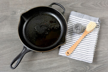 Dirty cast iron skillet being prepared for cleaning with bamboo brush, Stainless steel scrubber and...
