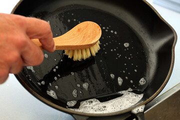 Close up A hand holding bamboo cleaning brush scrub and washing the dirty cast iron pan with a...