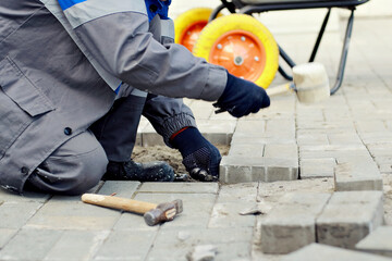 Bricklayer lays paving slabs outside. Working man performs landscaping. Builder lays out sidewalk with stone blocks. Authentic workflow. Hard work in old age.