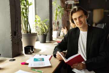 Young happy man looking at camera and smilling. Work in modern loft style office using devices and gadgets during job processing.