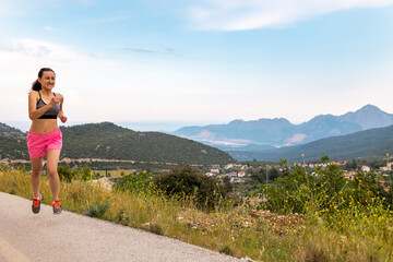 Naklejka na ściany i meble A girl runs along an asphalt road against the backdrop of beautiful mountains