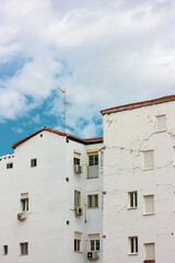 Fototapeta na wymiar Front view of old residential white houses against blue sky in nice day. Beautiful postcard of a city from a trip. Vintage Spanish architecture. Historic Quarter in town of Portugal. Cracked facades.