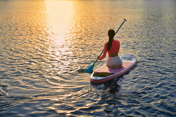Young female athlete spending evening time on city lake for practising in sup boarding. Beautiful...
