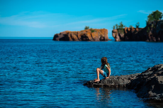 A girl on a rocky outcrop looks out over the water on a sunny summer day