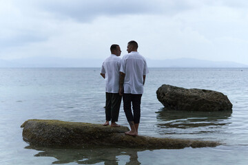 Gay couple looking to each other while facing the ocean int he evening