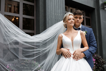 A wedding couple in love in front of a beautiful house. The blonde bride has a tiara on her head...