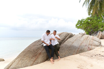 gay couple in white clothes talking on a rock beside the sea