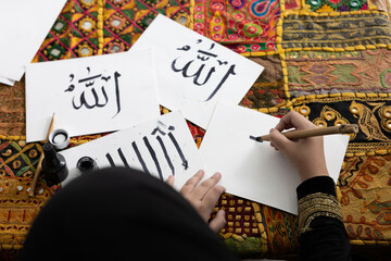 close up muslim girl hands writing Arabic text with bamboo pens and black ink on paper, Arabic letters mean the name of Muslim god 