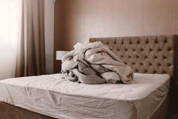 Big pile of beige linen lies on bed in domestic room. Housekeeping concept
