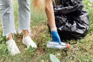 Young millennial caucasian woman cleaning-up public park or forest of plastic garbage. Volunteer picking up plastic bottle in woods. Green and clean nature, avoid pollution, be friendly to the