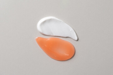 White cream and coral gel or lotion or serum swatches. Beauty routine concept. Different skin care products sample. Cosmetic smudge on grey background closeup. Top view.