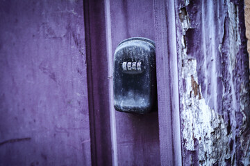 Old black mechanical coded door lock on purple door and peeling plaster wall