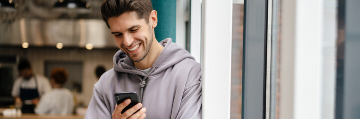 Happy young brunette man holding mobile phone