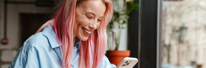 Young beautiful woman with pink hair using mobile phone in cafe