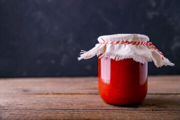 Tomato sauce on a black background. Seasonal preparation of vegetables in glass bottles on a wooden table. Traditional homemade recipes. Rustic food. Place for text