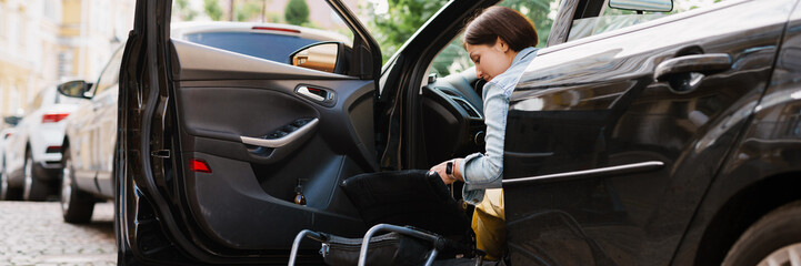 Brunette woman holding wheelchair while getting into car on city street