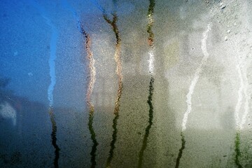 Transparente nasse Glasfläche mit Wasserstreifen und Sonneneinstrahlung  vor blau-braun-grauem...