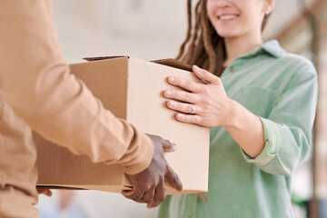 Close-up of smiling girl in casual shirt receiving big cardboard box from Black delivery man