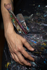 Close-up of the hands of an unrecognizable Latin American artist in apron showing the palette knives and brushes she uses to paint in her art studio. Artist and hobby concept