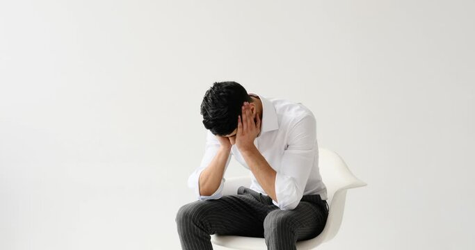 Depressed man feeling restless while sitting against white background