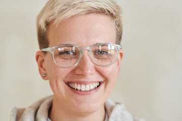 Portrait of positive attractive tomboy girl with short blond hair wearing glasses against isolated...