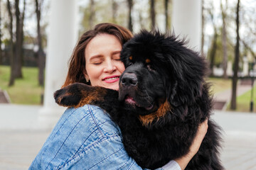 Woman hugging tibetan mastiff dog outdoors. Girl and dog playing in park - obrazy, fototapety, plakaty