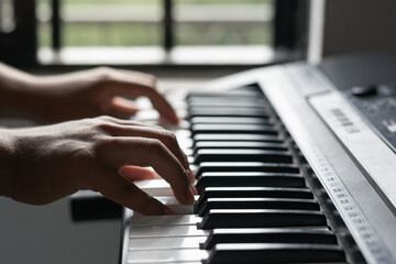 Fototapeta na wymiar young latin man creating a song on a synthesizer. detail shot of a musician's hands playing piano. hobbies at home in natural daylight. musical concept.