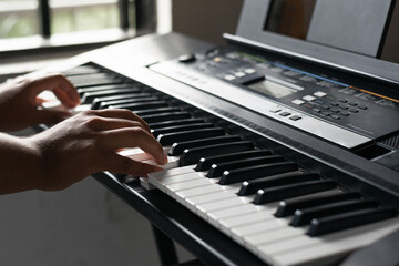 detail shot of a young latin guy practicing low and high piano notes on a synthesizer. boy taking...