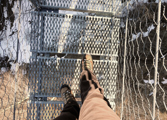 lightweight boots of man on the spectacular suspension bridge made of steel ropes and metal sleepers - obrazy, fototapety, plakaty