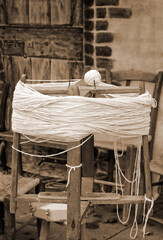 Fototapeta na wymiar antique wooden spinning wheel with a skein of wool below and a ball of yarn above with sepia effect