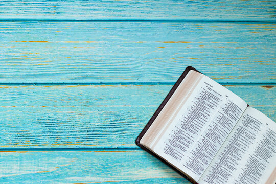Open Holy Bible Book on a blue wooden table background with copy space. Top view, flat lay. Christian biblical concept of Bible study, reading, and learning about God Jesus Christ. 