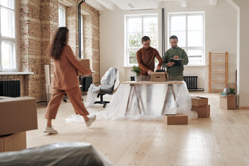 Group of young colleagues unpacking boxes while finishing moving into new office, blurred motion of...