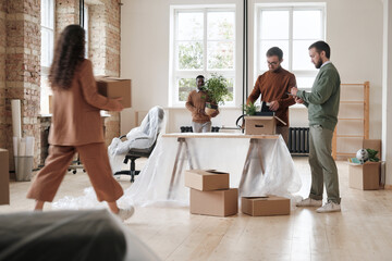 Group of men standing at desk covered with polyethylene and unpacking stuff while their colleagues...