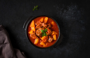 Stew with potatoes, in tomato sauce, with spices and herbs, close-up, no people, on a black background