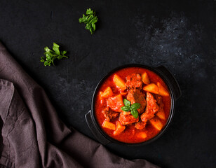 Stew with potatoes, in tomato sauce, with spices and herbs, close-up, no people, on a black...