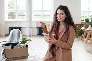 Portrait of smiling beautiful young woman eating Chinese food in new office with moving box on table