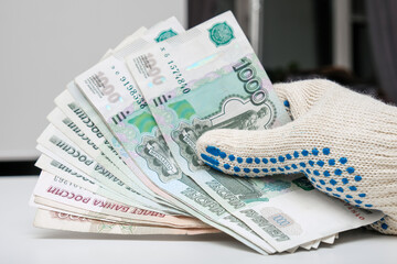 Hands of a worker, handyman, builder in protective gloves holding money, salary, payment for work in russian roubles