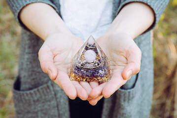 Close up view of woman hands holding and using Orgonite or Orgone pyramid. Converting negative...