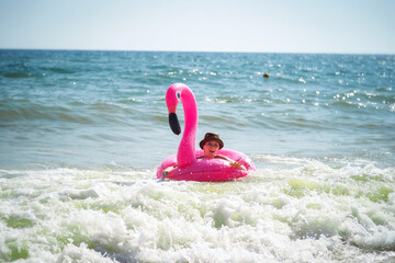 Pink inflatable flamingo. A girl is swimming in the sea. Sea waves. Cheerful mood. Vacation at the sea.