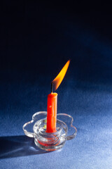 a small orange candle in a transparent candlestick burns on a blue background