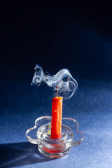 a small orange candle has gone out and is smoking on a blue background