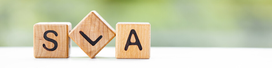 SLA - word is written on wooden cubes on a green summer background. Close-up of wooden elements.