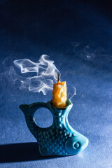 a yellow candle with a honeycomb texture is extinguished in a candlestick in the shape of a fish on a dark background and is smoking