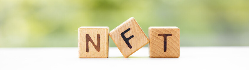 NFT - word is written on wooden cubes on a green summer background. Close-up of wooden elements. - obrazy, fototapety, plakaty