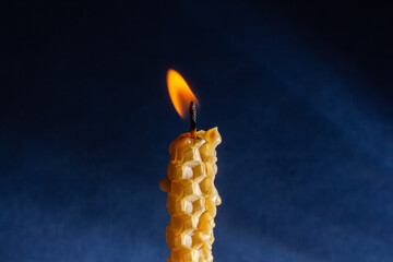 a yellow candle with a honeycomb texture burns on a dark background