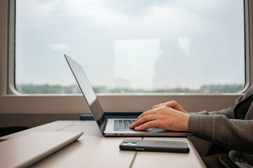 Men's hands type on the keyboard of a silya laptop on a train. European trains, travel, smartphone. Digital work, digital nomad. High quality photo