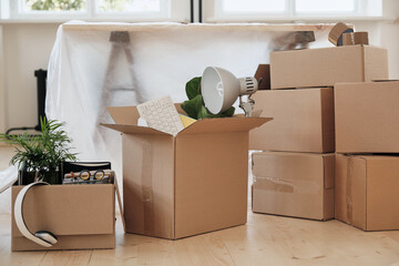 Abundance of moving boxes stacking on floor against table covered with polyethylene in new office