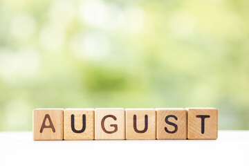 The word August on wooden cubes. They lie on other cubes against the backdrop of the summer garden....