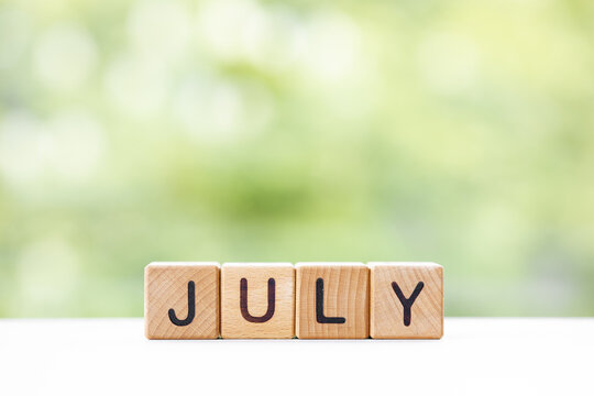The word July on wooden cubes. They lie on other cubes against the backdrop of the summer garden. Month of year
